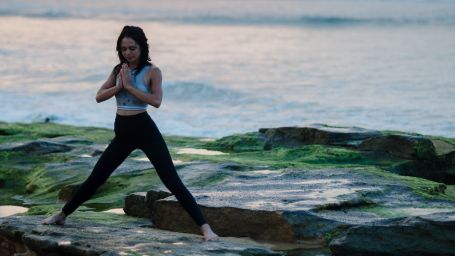 a girl performing a yoga asana on rocks near the beach with the sunset sky in the background