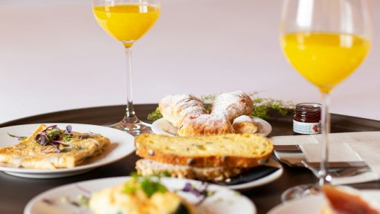 A room service breakfast tray with orange juice and an assortment of breakfast foods on a bed