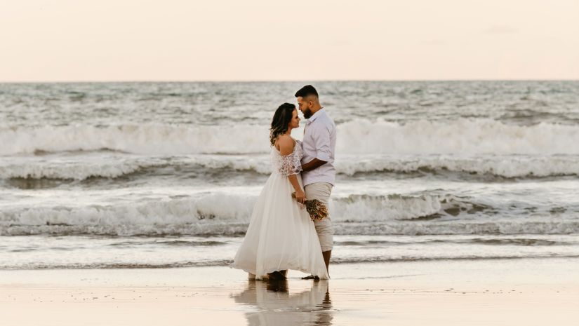 A newly wedded couple hugging in the backdrop of a beach