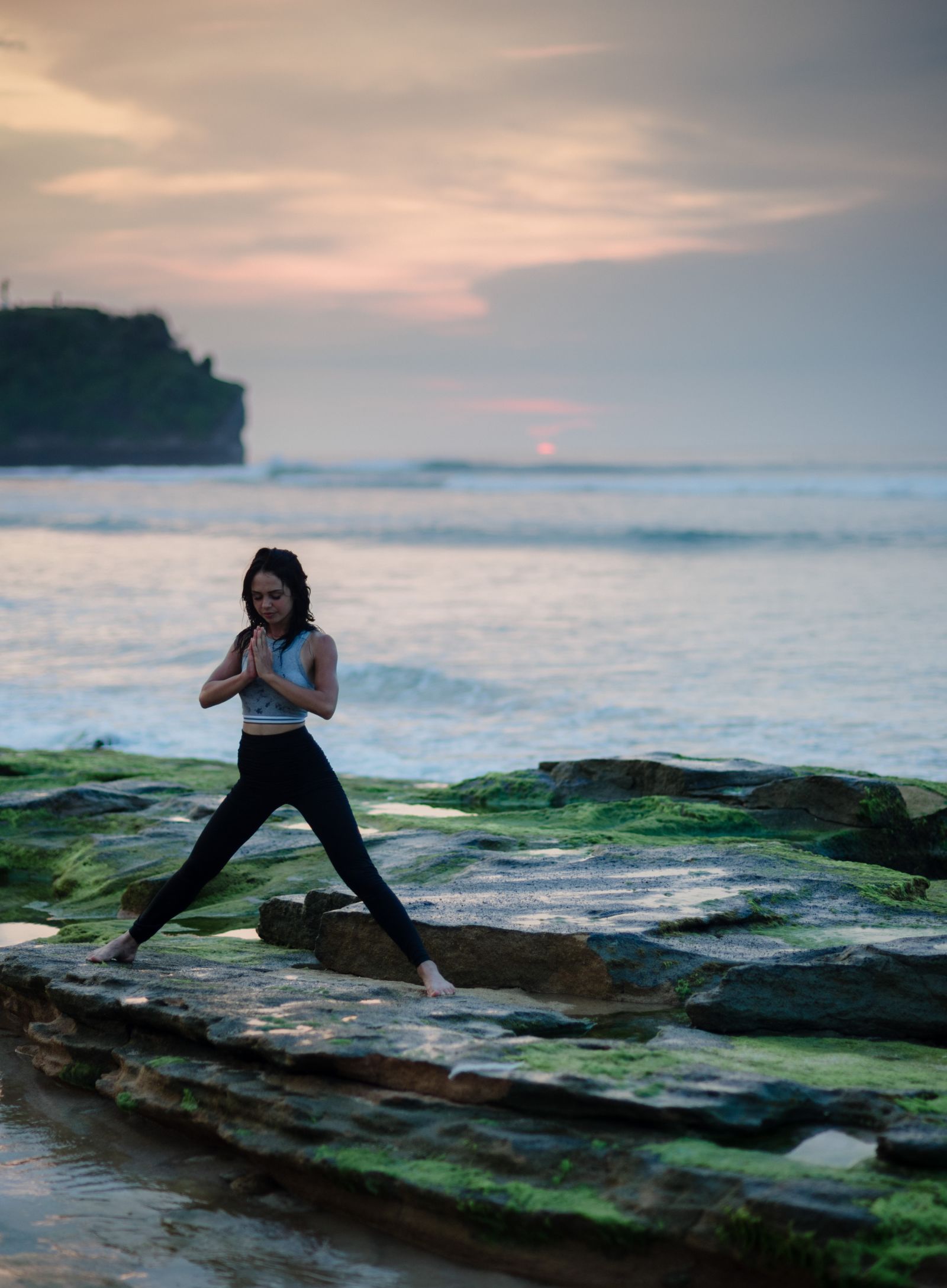 a girl performing a yoga asana on rocks near the beach with the sunset sky in the background