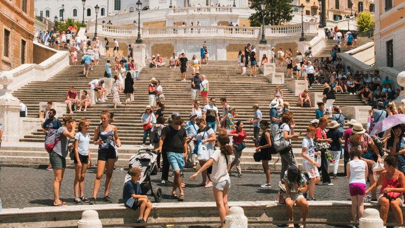 many tourists walking and sitting on a flight of stairs outdoors with a fountain in the foreground