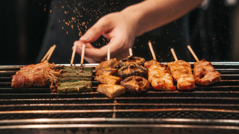 A man sprinking salt over pieces of meat in skewers