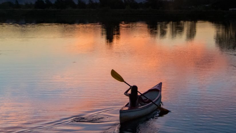 A person kayaking on a river with the sun setting behind it