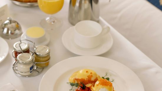 Gourmet breakfast on a hotel bed with eggs Benedict and a pastry selection