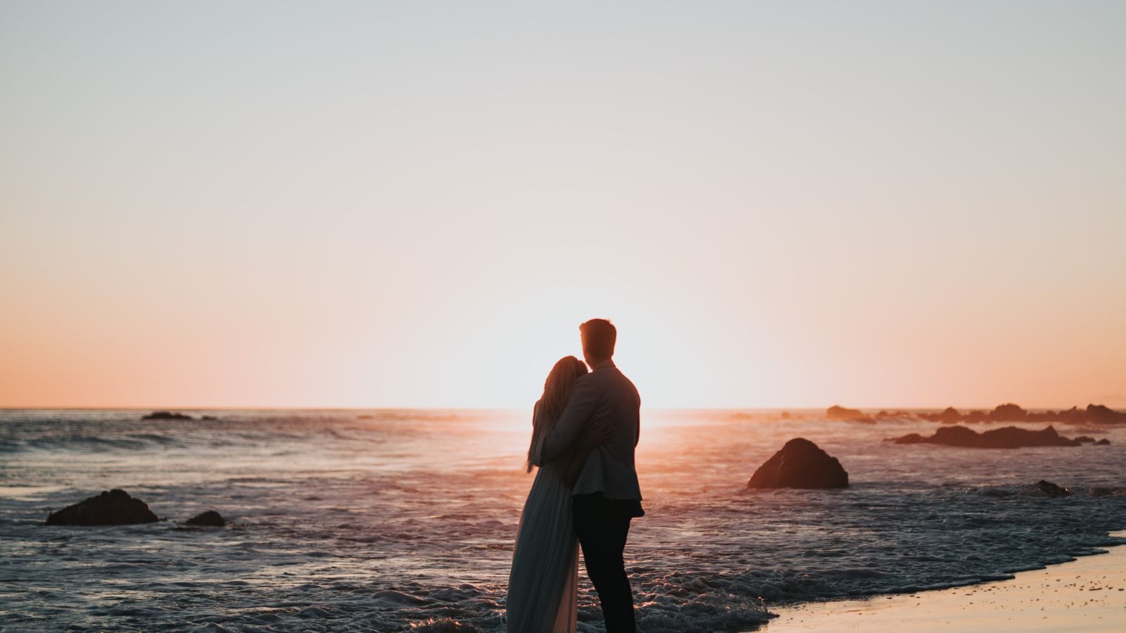 a couple watching the sunset on a beach while the waves overlap on their feet