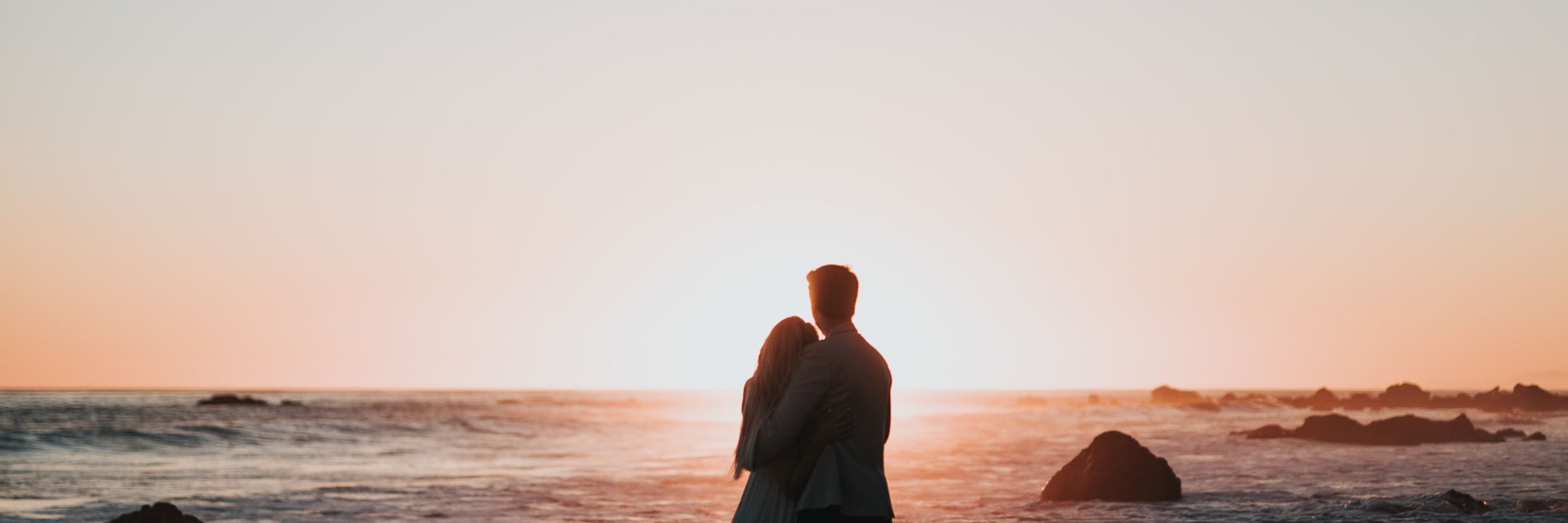 Couple hugging on the beach looking at sunset