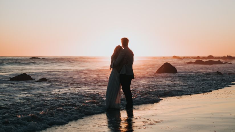 a couple hugging each other with the sun setting in the background