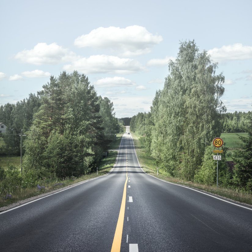 an empty road amidst trees with blue skies in the background and white clouds as well