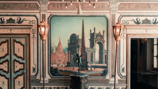 a small statues of a man doing a pose in front of a painting and a chandelier hanging from the roof