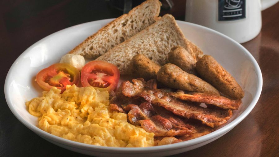 a plate with breakfast items and a coffee mug kept next to it on a table