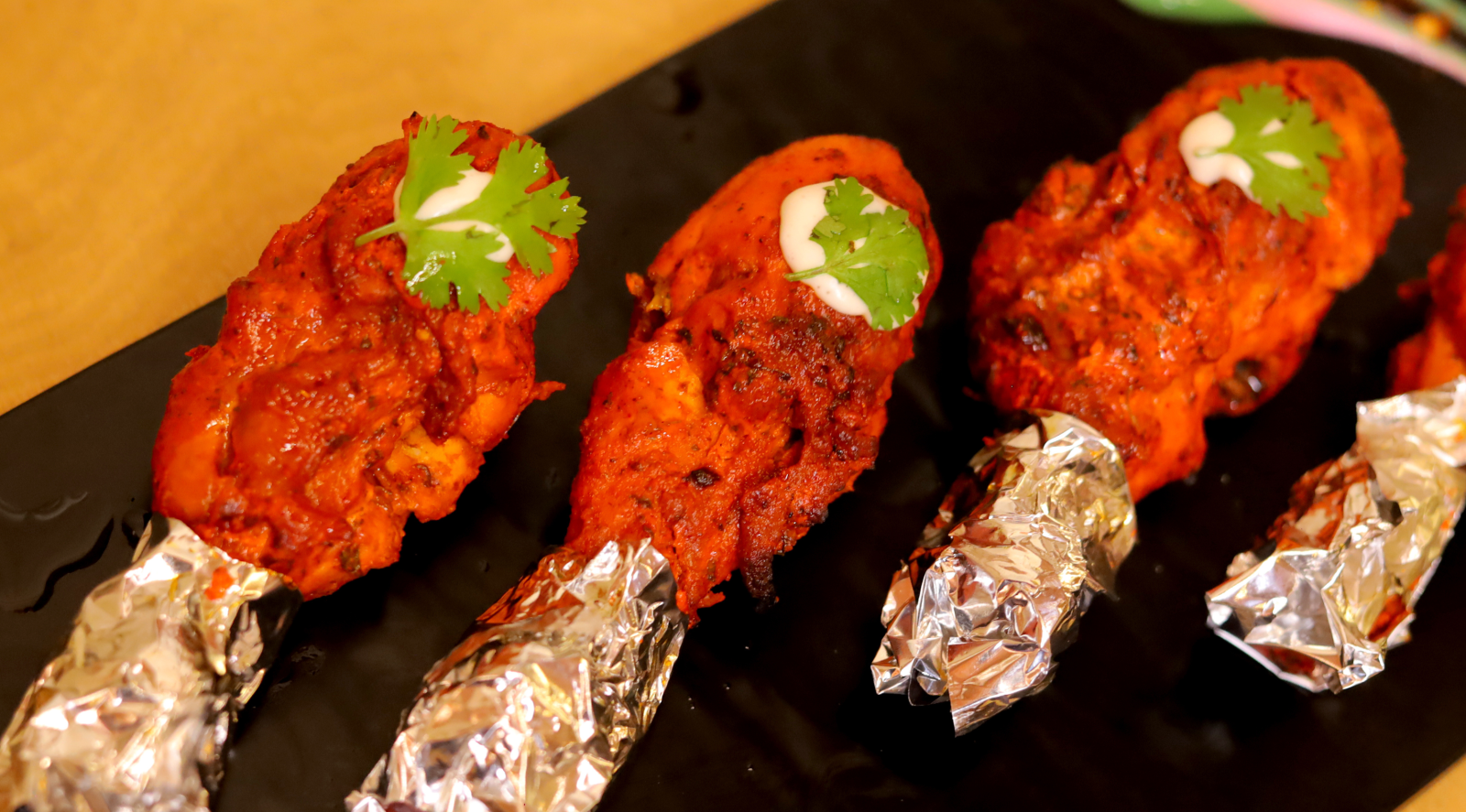 Tandoori chicken drumsticks garnished with cilantro leaves served on a black platter at Themis Barbecue House.