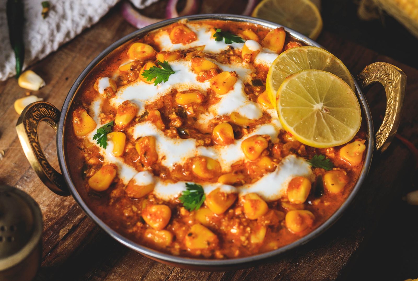 A traditional Indian dish garnished with cream and served in a brass bowl with lemon on the side