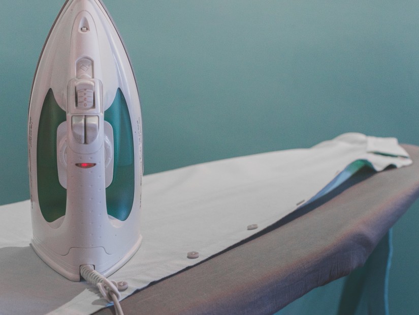 a close up image of an Iron and ironing board with a blue wall in the background