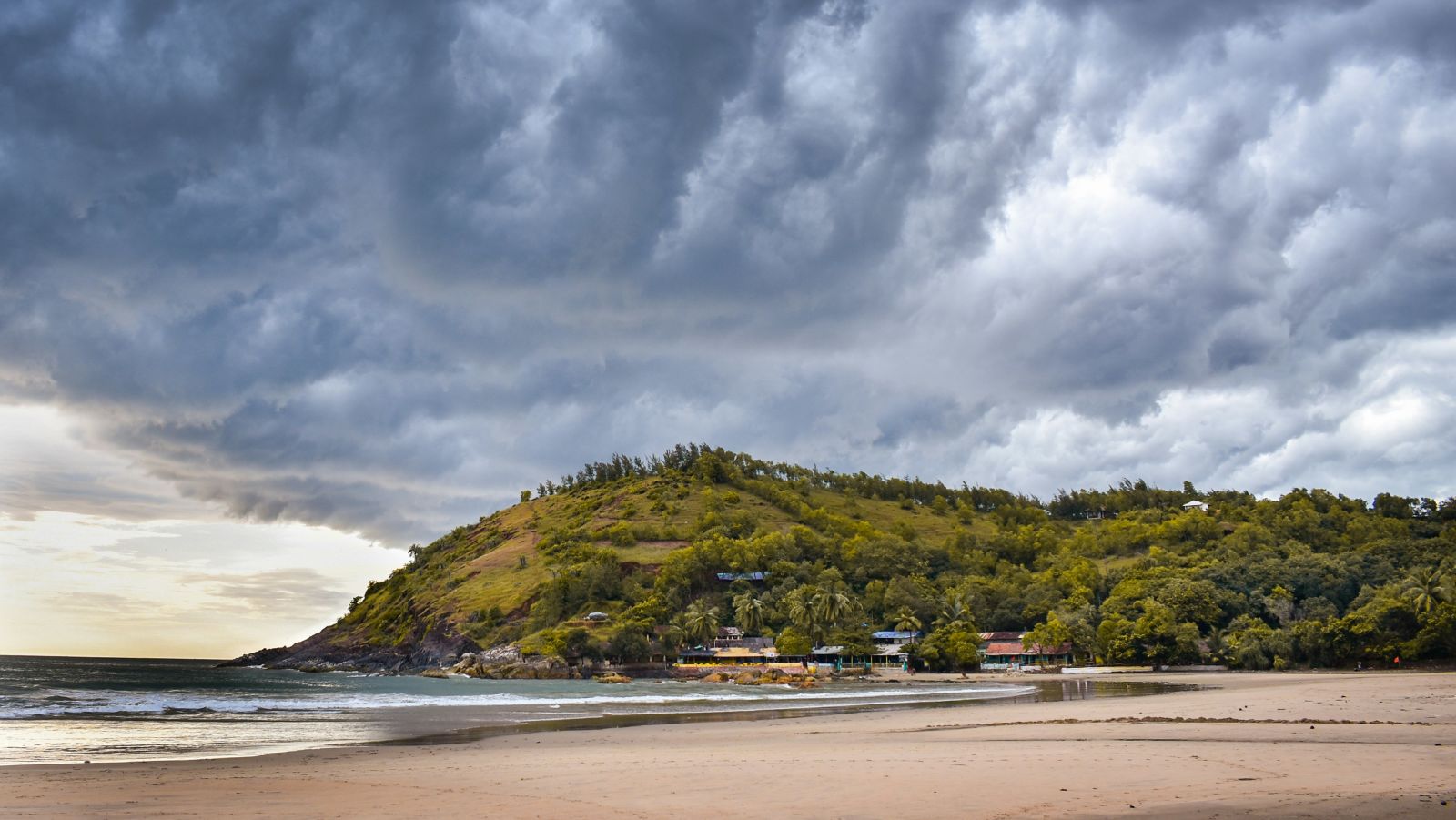 A pristine beach with water overlapping the sand and a small green mountain in the background