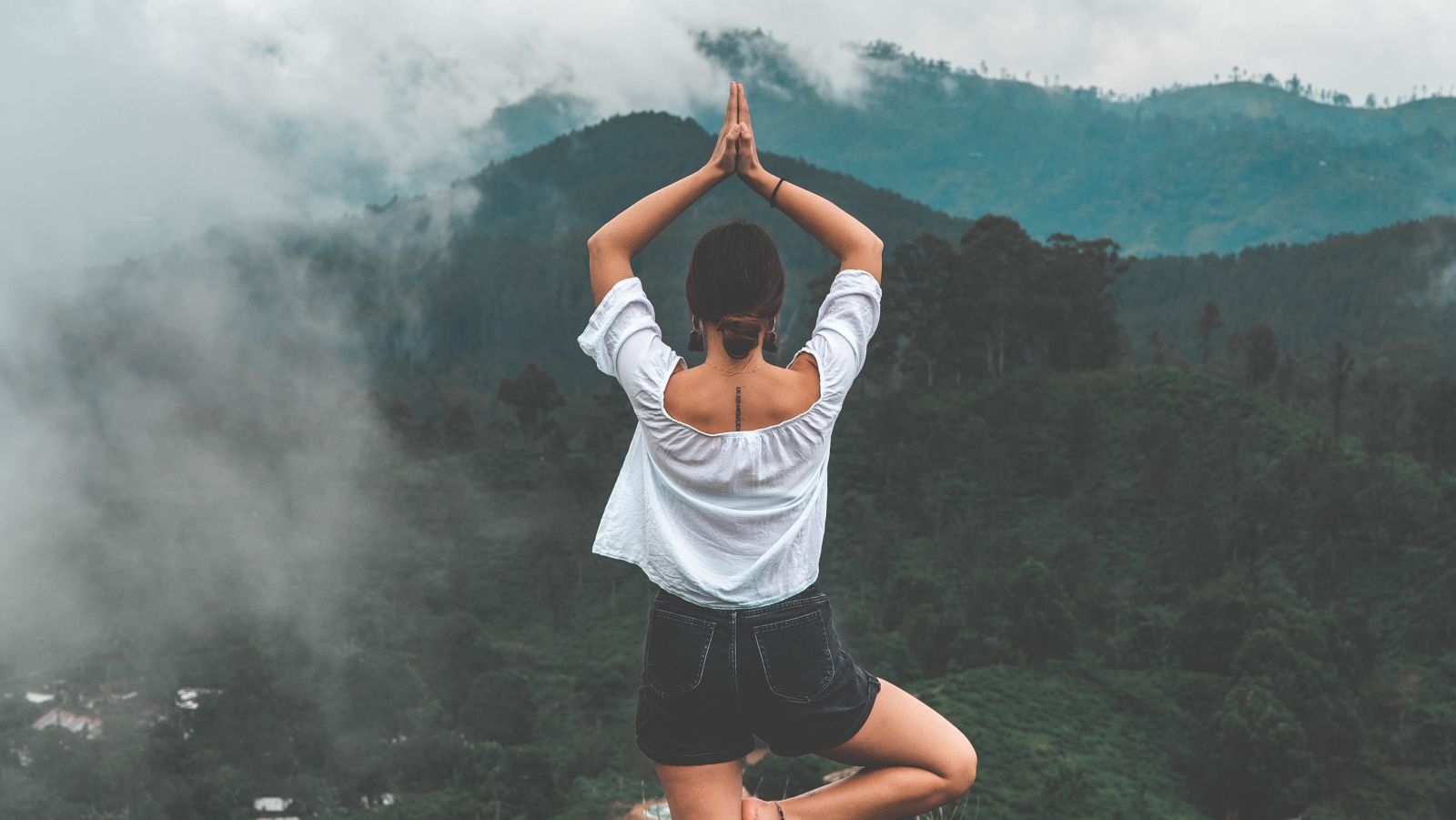 A woman in Vrksasana yoga pose amidst the mountains during daytime