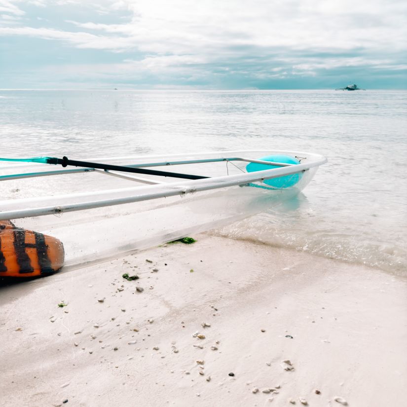 a glass bottom boat on the beach next to the sea with blue skies covered in white clouds in the background