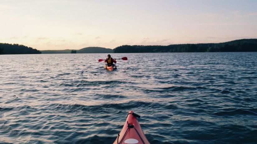 a POV of a person kayaking of another person kayaking in front of him with land in the background