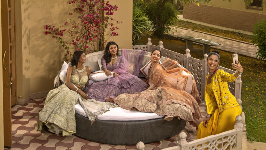 alt-text A group of women enjoying tea in a cozy garden setting with lush greenery, comfortable pillows, and ornate furniture at dusk.