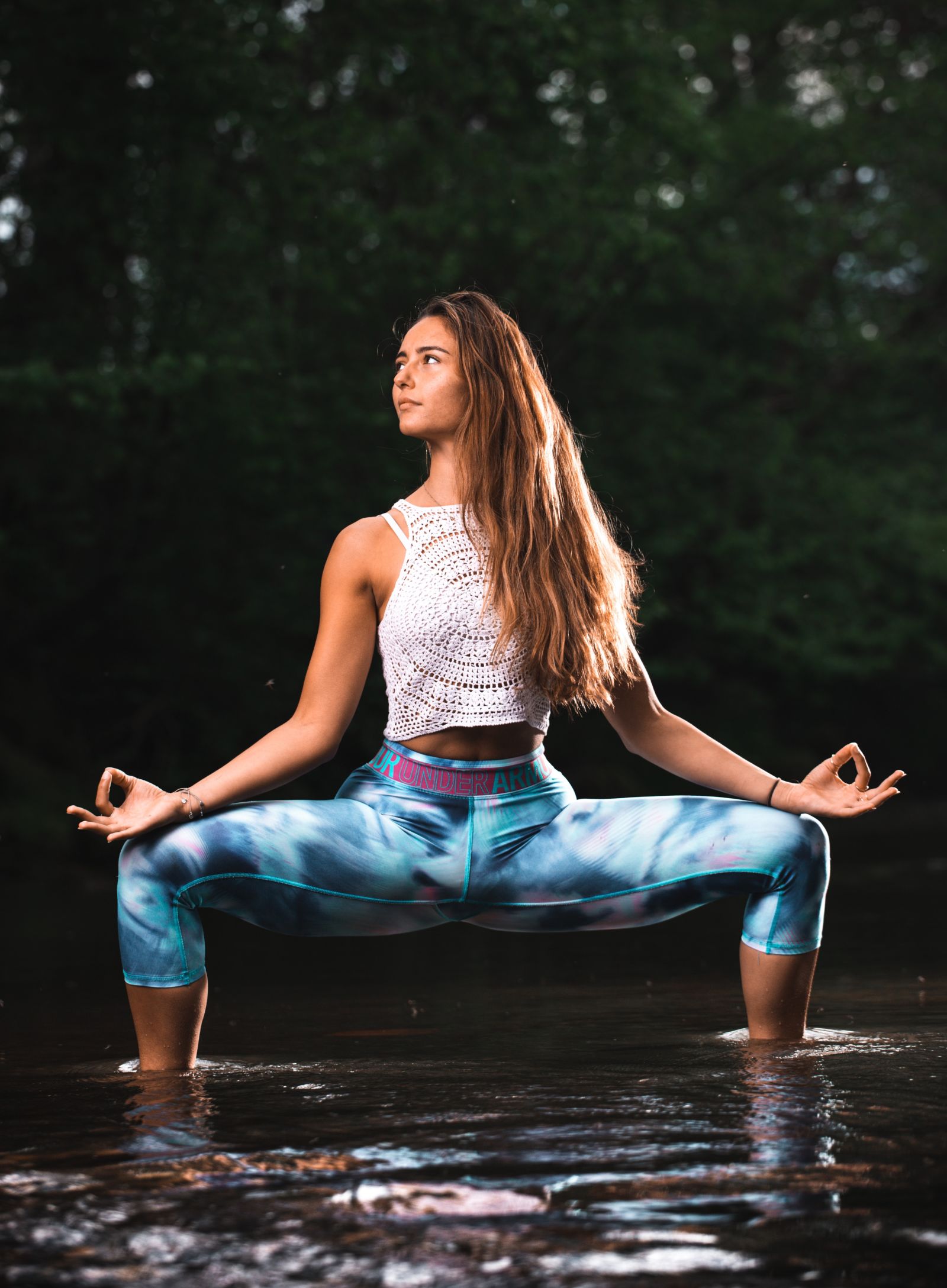 A girl performing a yoga asana standing in a water body with trees in the background