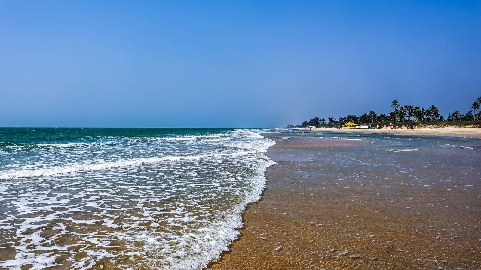 Foamy Waves flowing over the sand at varca beach with beach umbrellas in the background