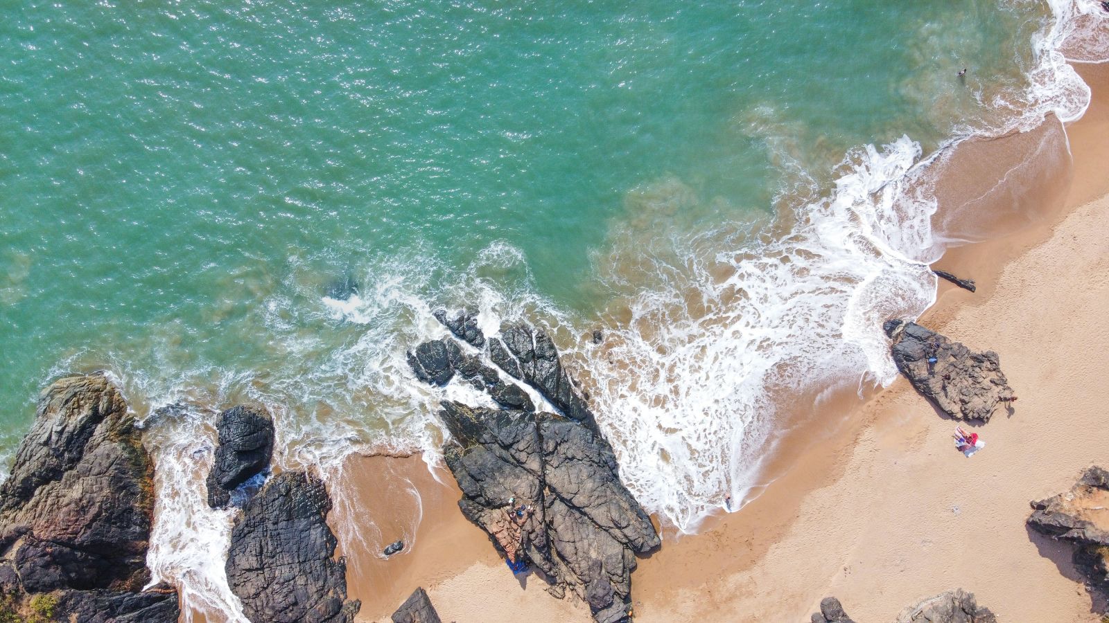 a bird's eye view of a beach with rocks on it and water overlapping the sand