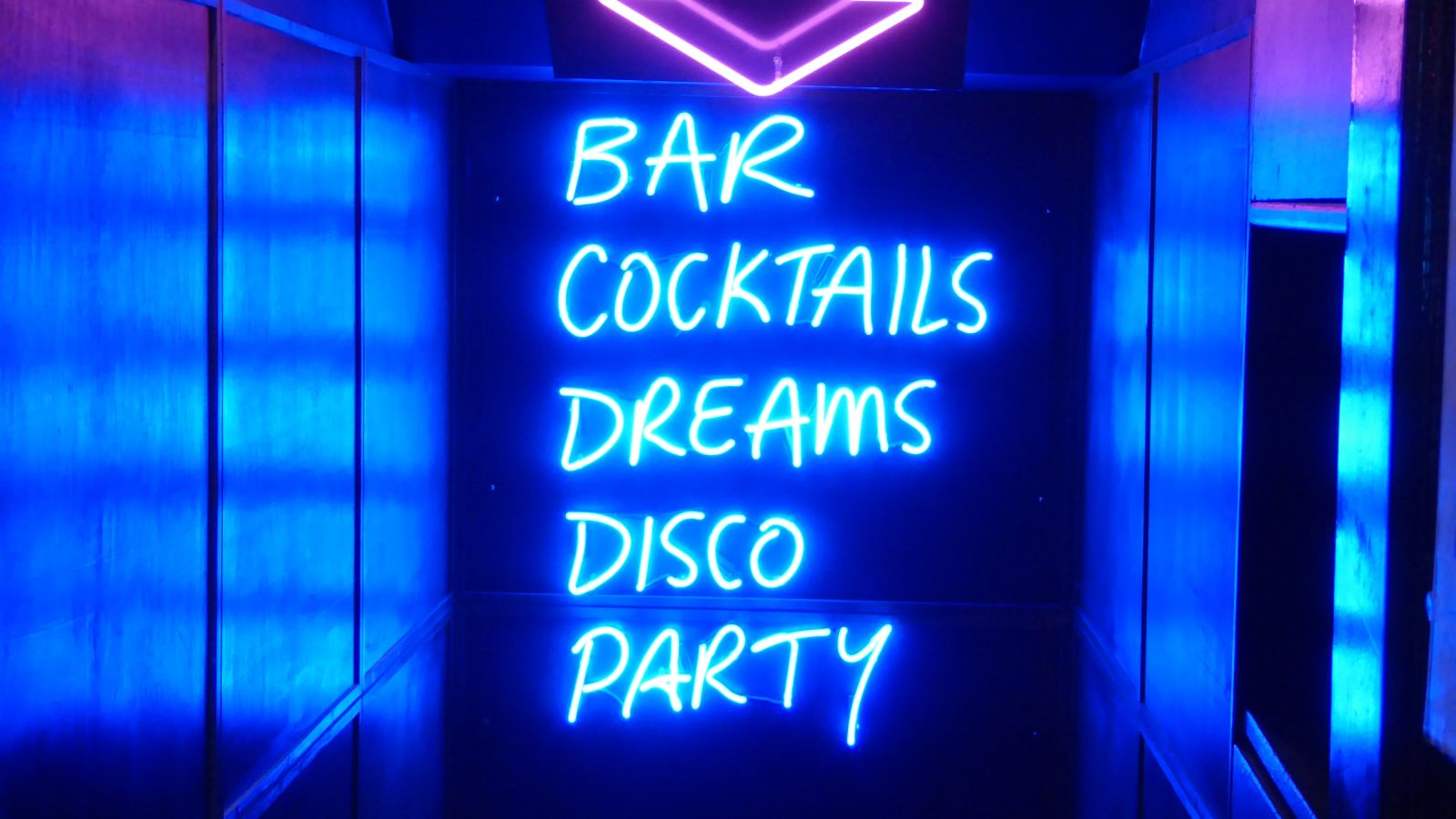 Party board sign outside a club with the words bar, cocktails, dreams, disco and party written on it