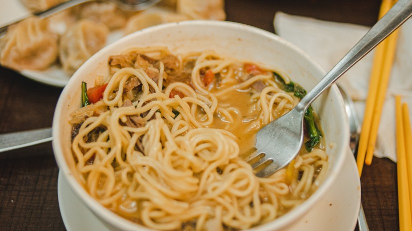 a bowl of thukpa with a plate of momos in the background