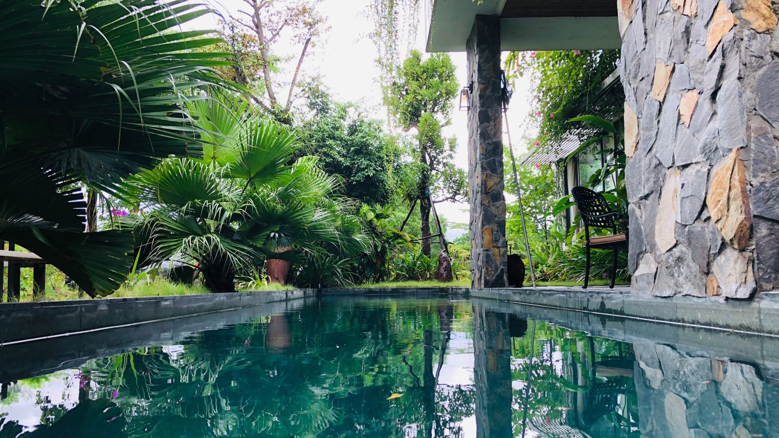 A swimming pool beside a stone wall and trees on the side - Caravela Beach Resort Goa