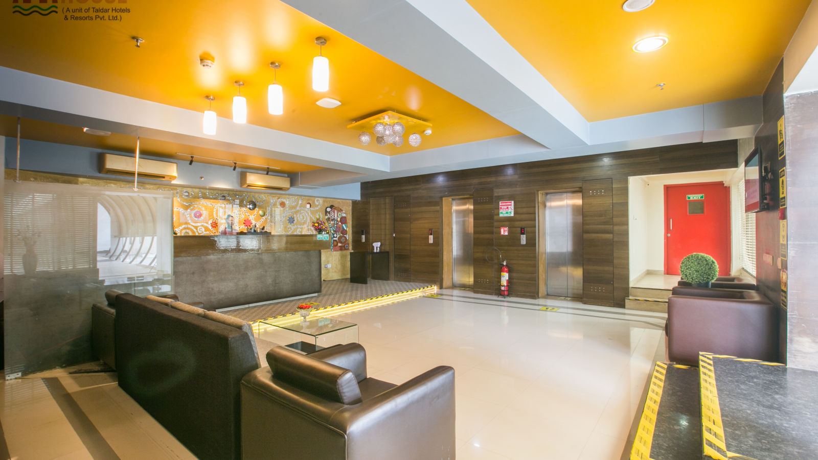 Spacious lobby with bright lighting, modern furniture, a vibrant yellow ceiling, and elevators.