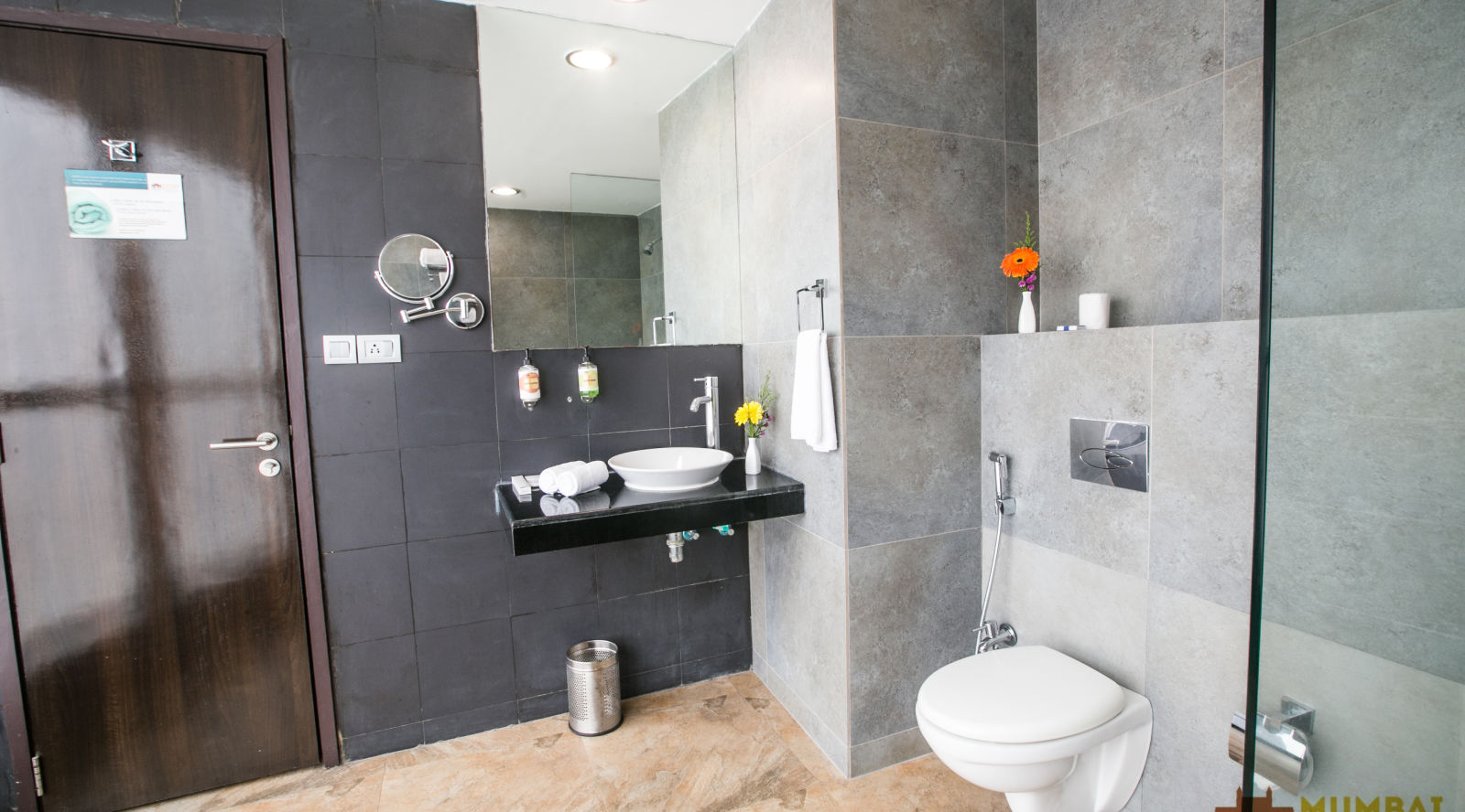 Contemporary bathroom featuring a toilet, a mirror, a sink with amenities, and grey tiled walls.