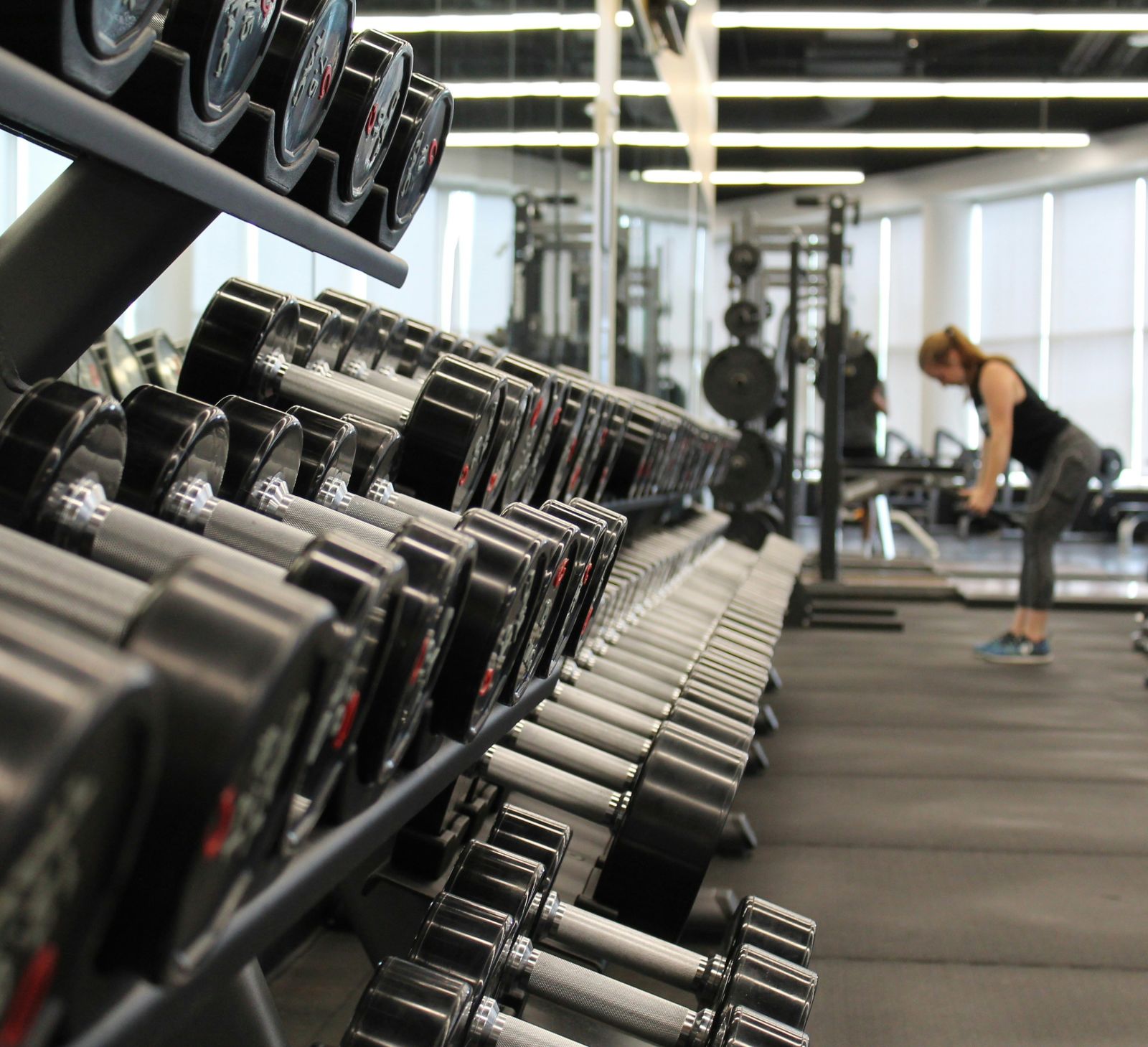 A close up shot of dumbbells in a rack with a person in the background working out