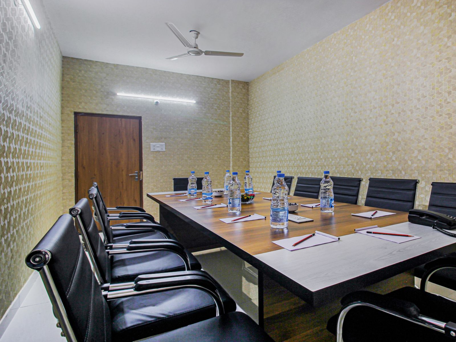 A meeting room with a professional setting, featuring a large meeting table with water bottles and notepads for attendees.