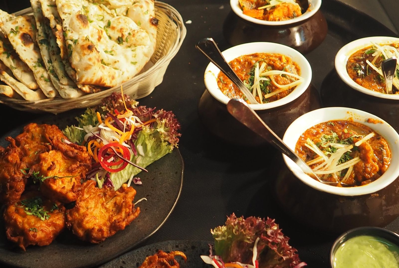 A variety of Indian dishes including naan bread, pakora and several curries served in small bowls