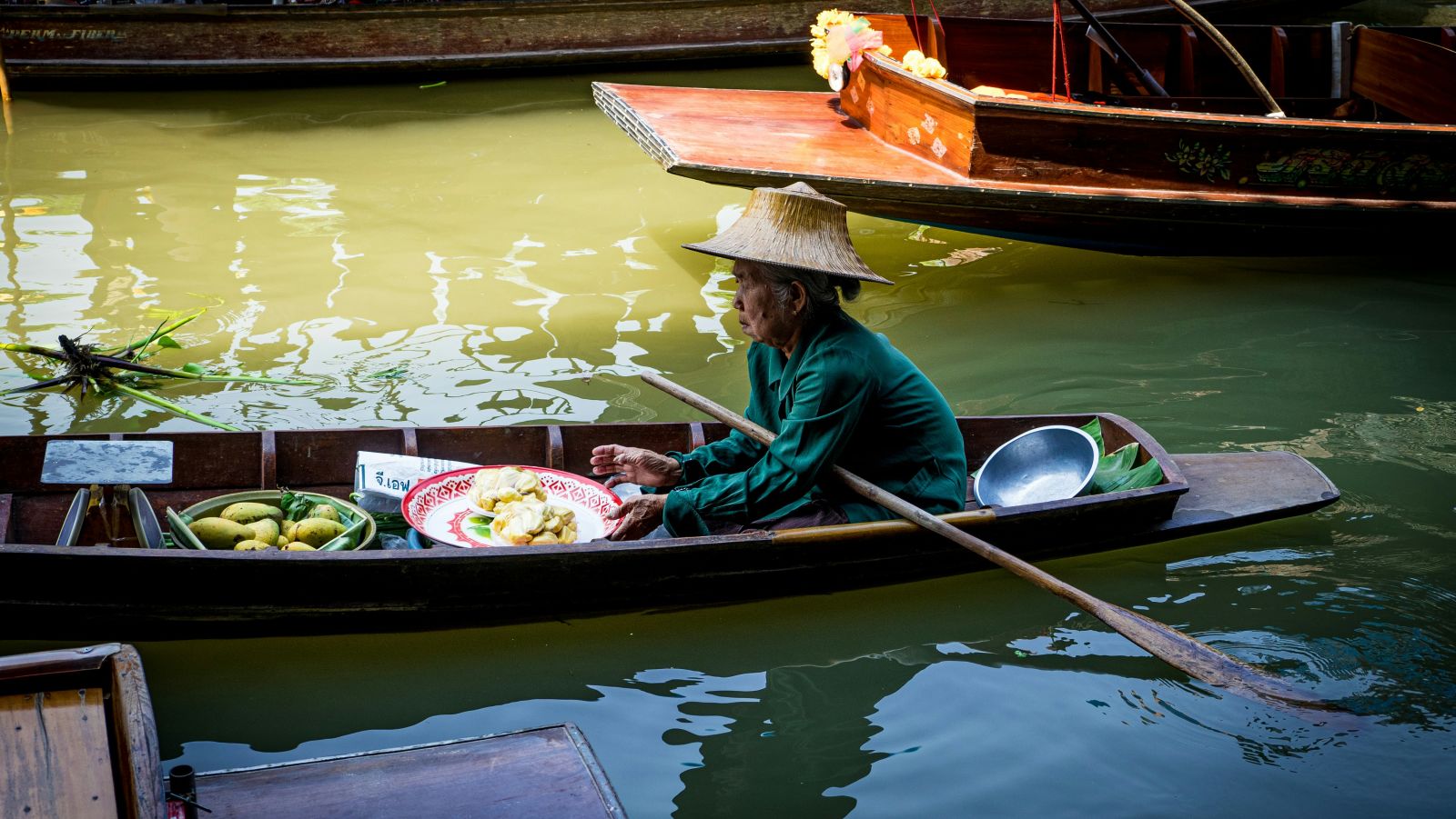a seller holding an oar and looking into the distance while being in a floating market