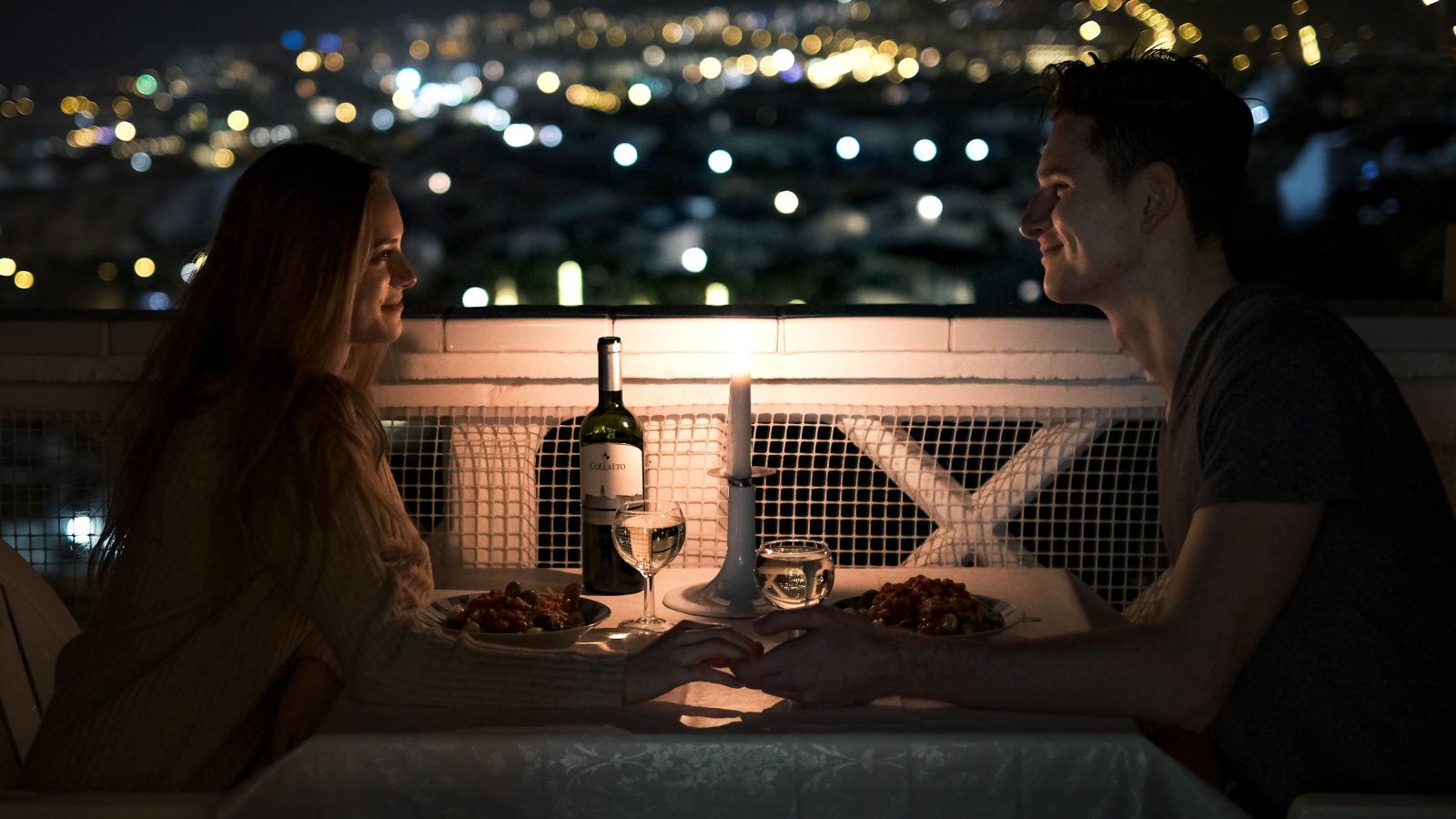 A romantic couple dinner with lights of the city in the background