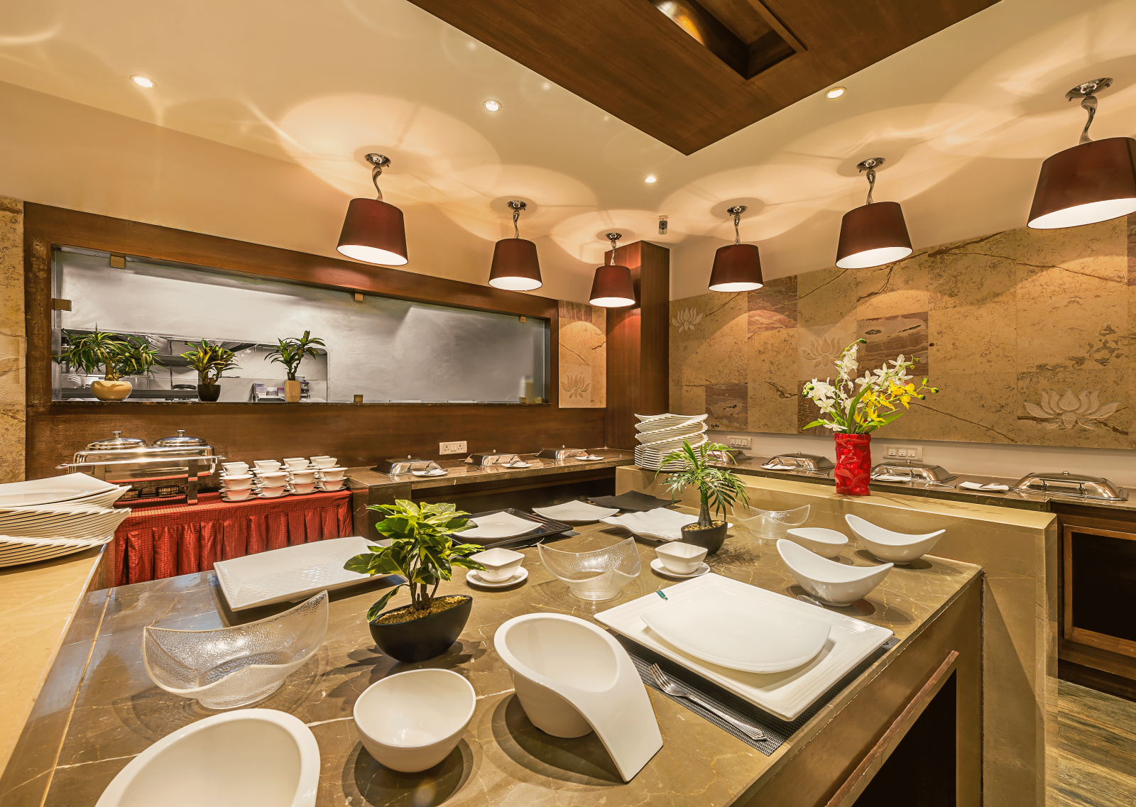 Elegant buffet area in a restaurant with wooden accents, red lampshades and a variety of white serving dishes arranged for use - TGI Grand Fortuna, Hosur