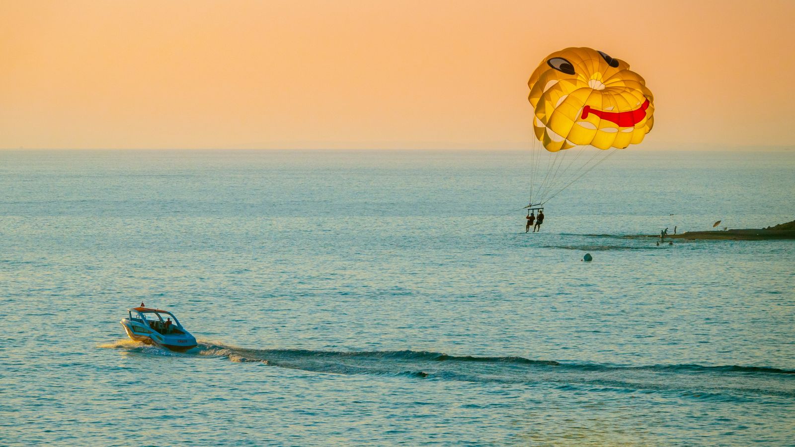 a boat travelling on a waterbody while parasailing two people behind