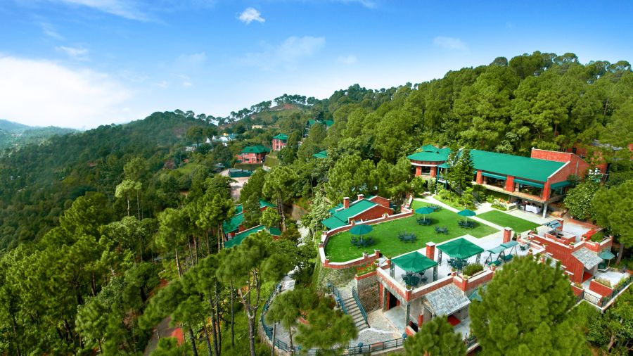 a drone shot of the hotel with the property covered with and surrounded by trees - Baikunth Resort, Kasauli