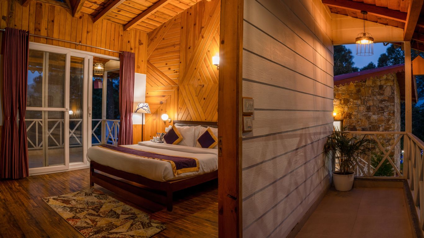 A room with a well made bed, expansive windows and an attached balcony - The Nature's Green Resort, Bhimtal