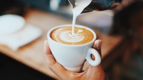 a woman holding a cup of coffee and pouring milk in it