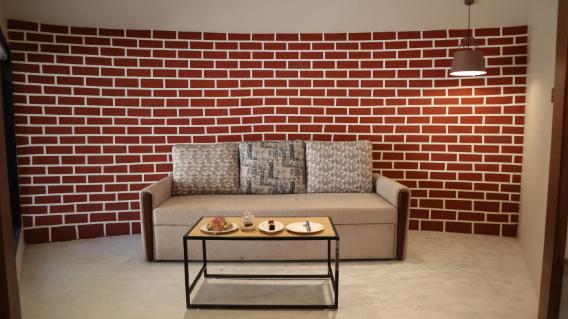 A sleek glass coffee table and a comfortable grey sofa are paired in a stylish living room with exposed brick walls - Jagira Ananta Elite Gir