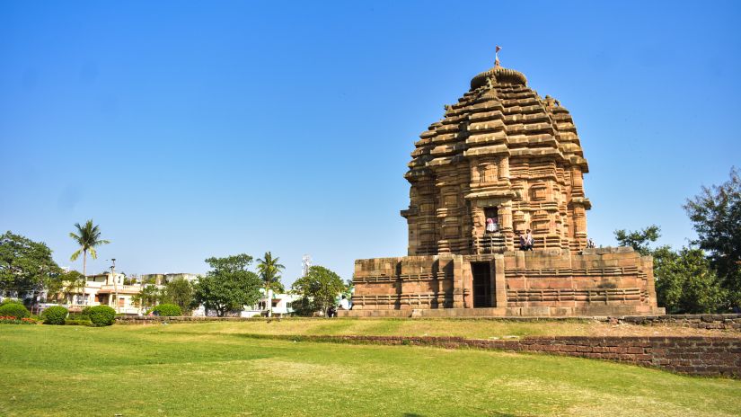 An ancient temple with intricate designs, set against a clear blue sky in a well-maintained grassy field, reflecting the grandeur of historical architecture.