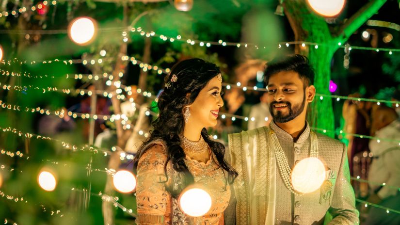 a couple posing with fairy lights lit at the back