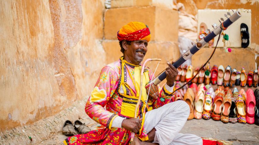 A colourful puppet show is playing in the background, as a musician dressed in colourful traditional garb plays a stringed instrument