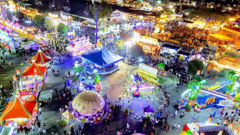 an aerial shot of an open area brightly decorated with vibrant colours with plenty of fun rides and crowded with people