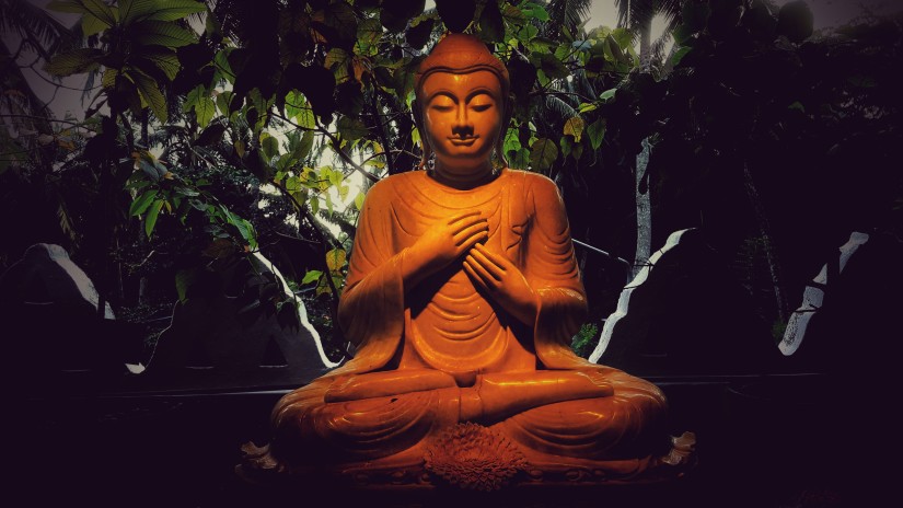 A statue of Buddha with rocks and greenery behind