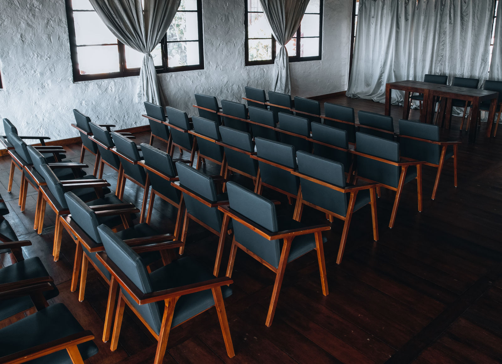 Banquet hall with rows of wooden chairs and windows with drapes.