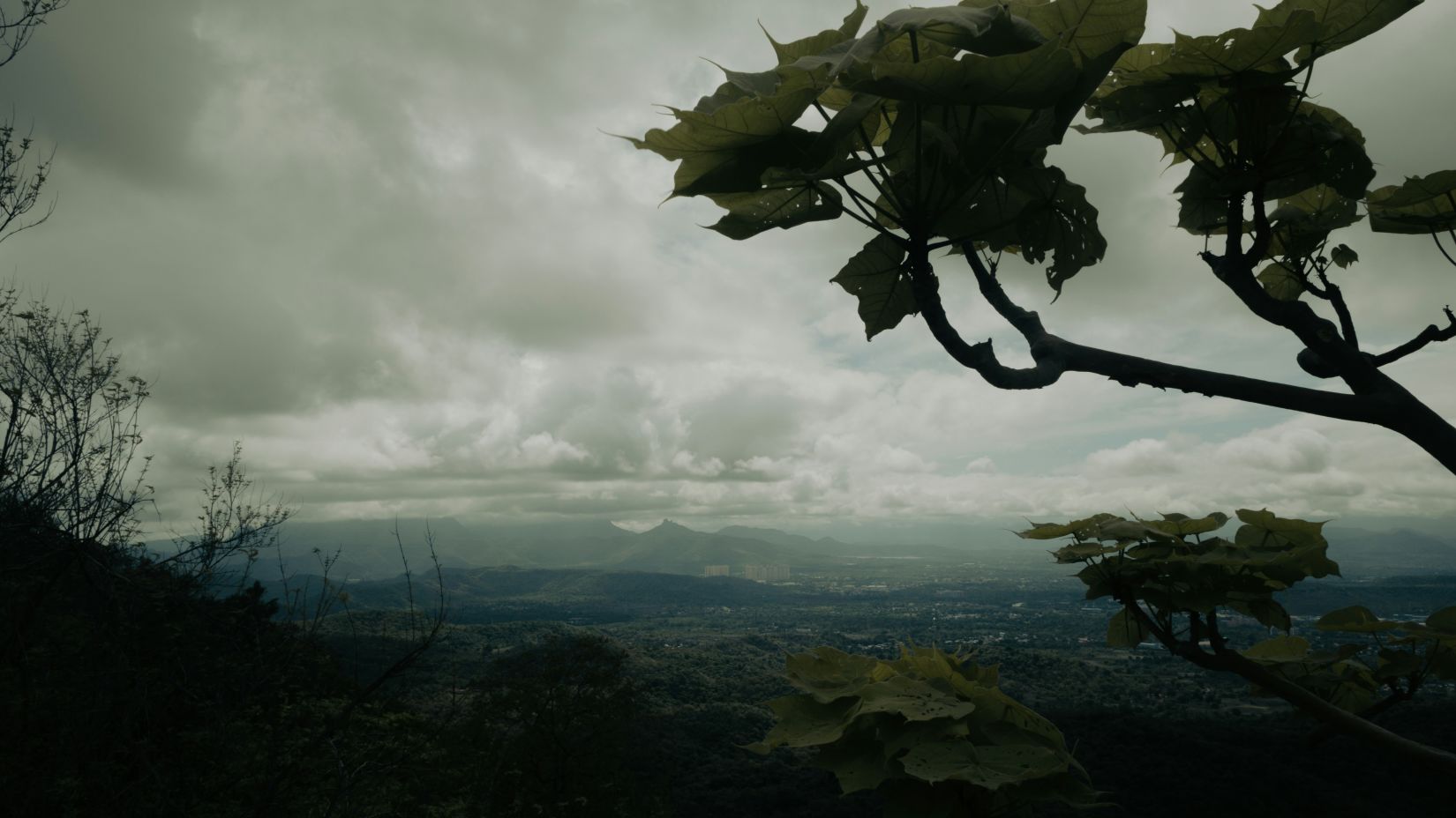  A moody landscape view from a hilltop featuring overcast skies and a sprawling valley with distant mountains. - Fort Jadhav GADH