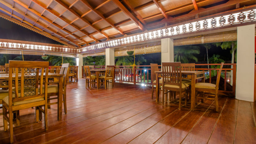 a beautiful restaurant surrounded by green palm trees, decorated by soft white lights and indoor seating- Symphony Summer Sand Beach Resort And Spa