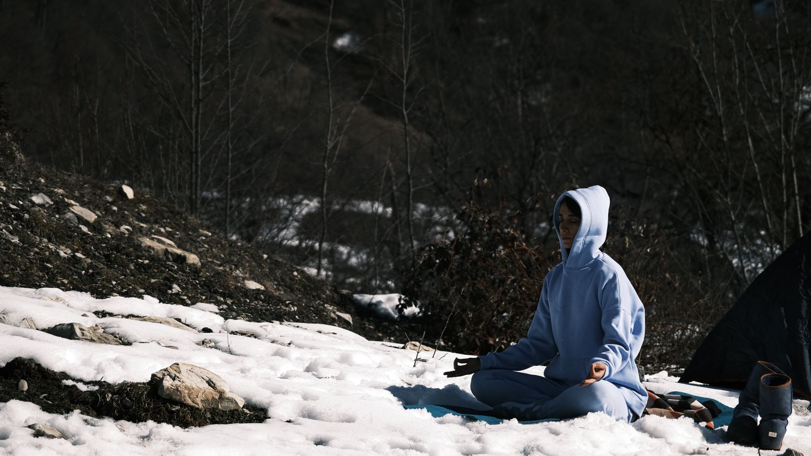 A person meditating amidst snow and rocks on the ground with boulders in the background